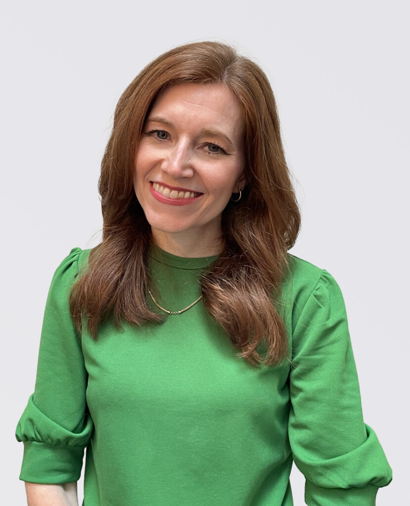 Professional headshot of a smiling woman with red hair in a green shirt